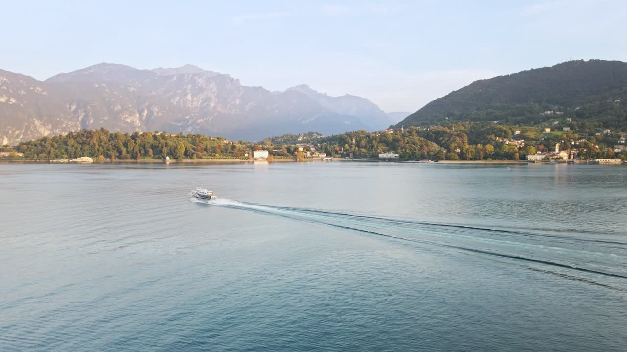 A stunning drone shot at Lake Como, moving forward as a boat heads towards Bellagio. The serene lake and majestic mountains in the backdrop enhance the breathtaking scenery.