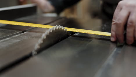 close-up as a carpenter uses a tape measure to measure and adjust the cut distance on a table saw