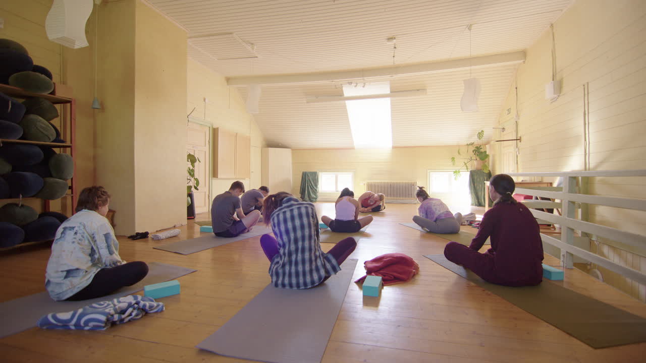 Siddende yogier i en gruppe yogatime vugger kroppene fra side til side, set bagfra.