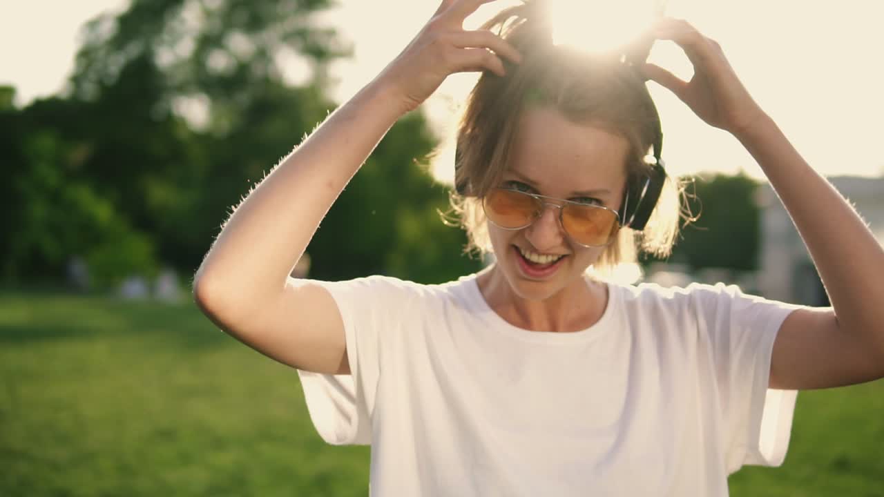 chica caucásica atractiva divirtiéndose al aire libre. posando y sonriendo a la cámara con camiseta blanca, auriculares en el cuello