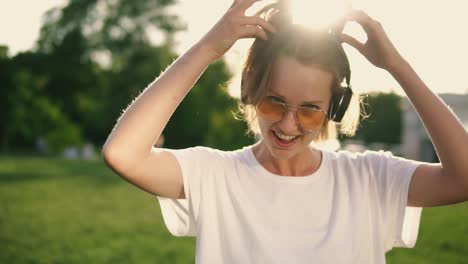 Attractive-caucasian-girl-having-fun-outdoors.-Posing-and-smiling-to-camera-wearing-white-T-shirt,-headphones-on-her-neck