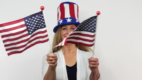 a woman sways two flags in ultra slow motion while smiling with a white background behind her