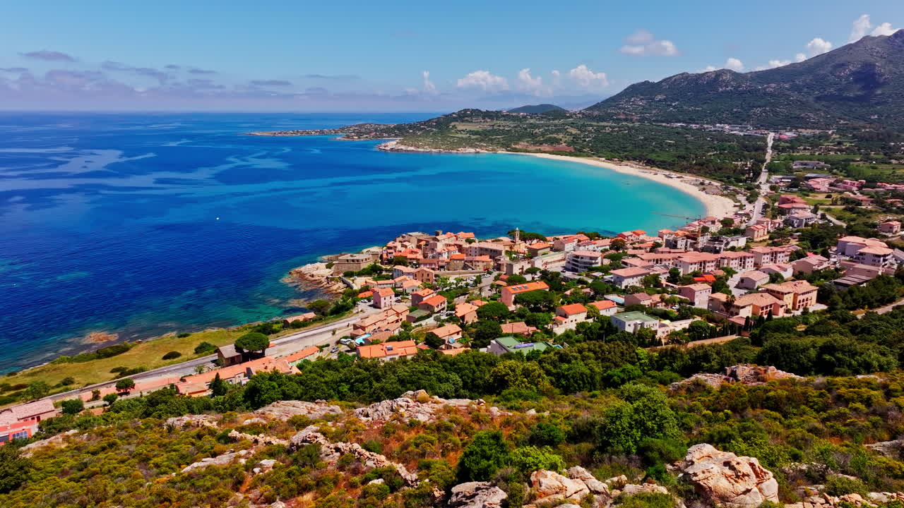 Aerial drone shot over the coastal town of Algajola in Balagne, Corsica, France. High view of the local town and the turquoise sea. Bright blue sky. Summer holidays destination