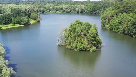 Peaceful-flight-over-a-calm-serene-lake-surrounded-by-a-forest-of-trees-on-a-clear-sunny-day-in-spring