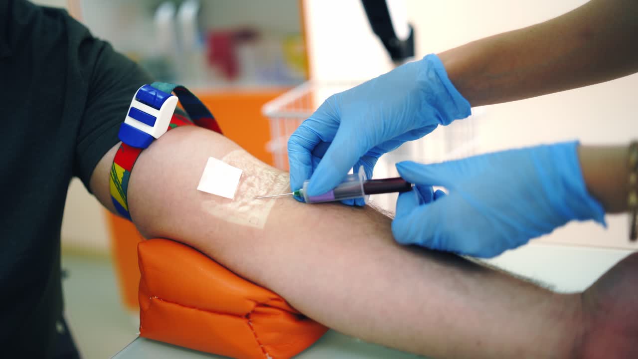 Nurse taking blood sample from vein. Close-up worker's hands in sterile gloves collecting blood with syringe into vial from patient's arm. Healthcare concept.