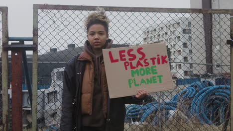 joven activista estadounidense sosteniendo un cartel de cartón contra el uso de plásticos durante una protesta por el cambio climático mientras mira la cámara