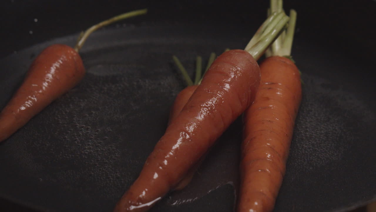 Orange roots falling into in a layer of water in a black pan. Close up slowmo shot