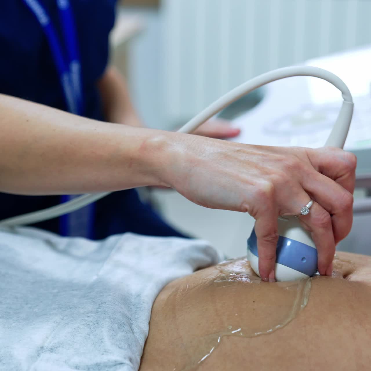 Pregnant patient is checked on the ultrasonic equipment. Obstetrician's hand moving transducer by the belly of female. Close up