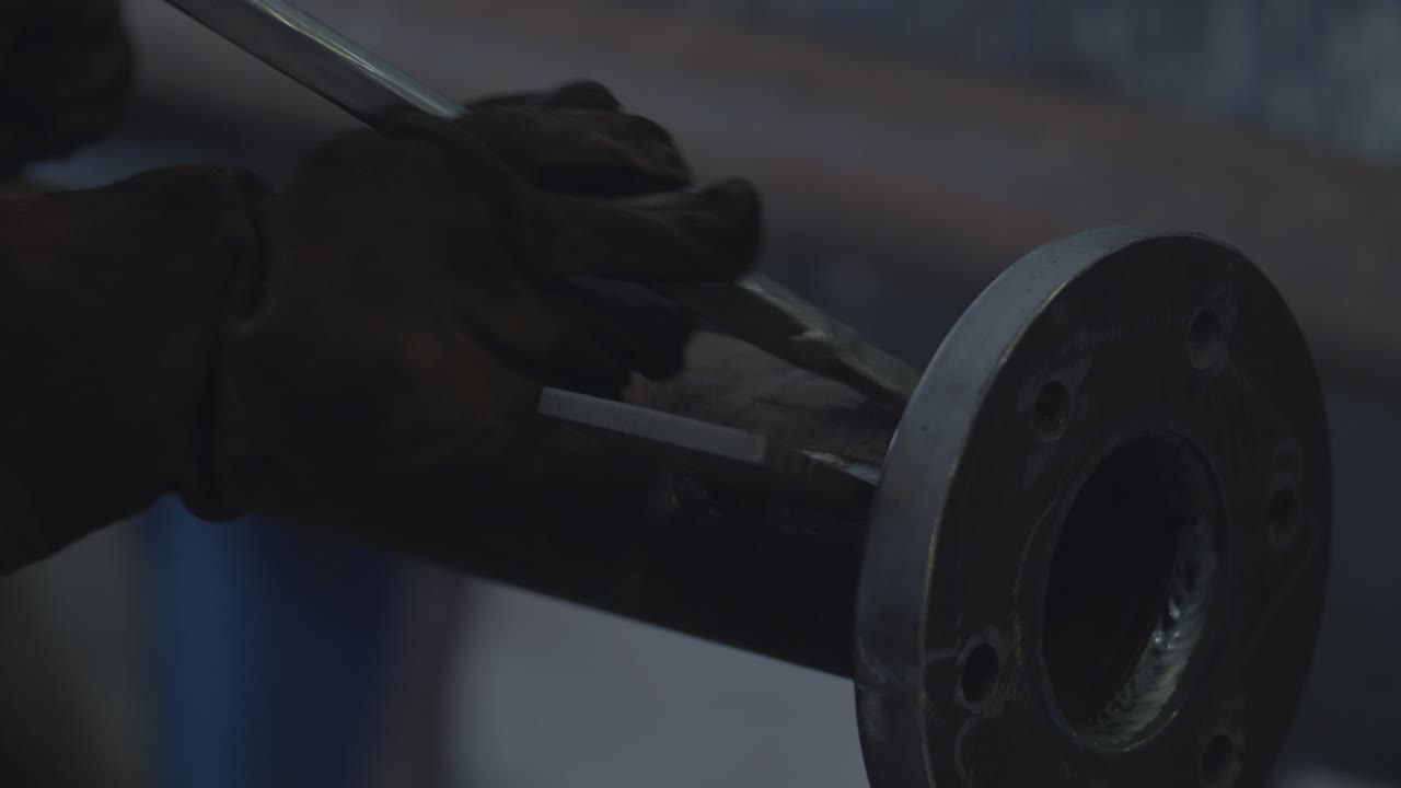 Worker uses metal bar to clean up the welding spot of a metal pipe.