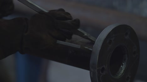 worker uses metal bar to clean up the welding spot of a metal pipe.