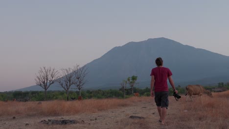 Man-walking-through-dry-savanna-in-Bali-with-Mount-Agung-in-the-background-during-sunset