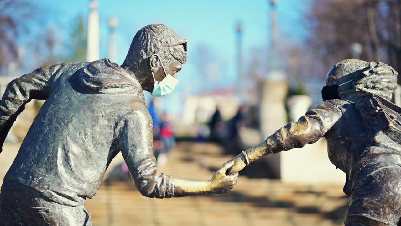 A beautiful bronze sculpture depicts two figures holding hands, both wearing masks in a city park. This artwork highlights the importance of connection during challenging times