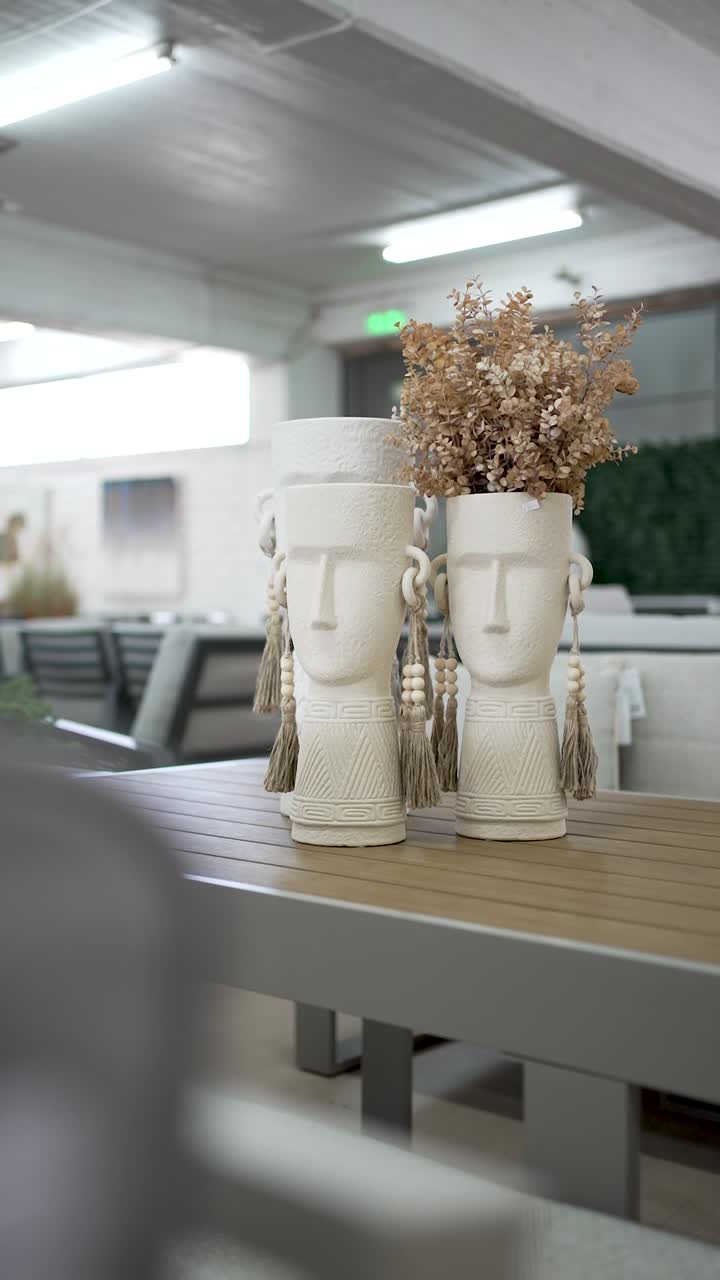 Two artistic white vases shaped like faces hold dried flowers, adding a touch of elegance to a stylish dining area decorated with modern furniture