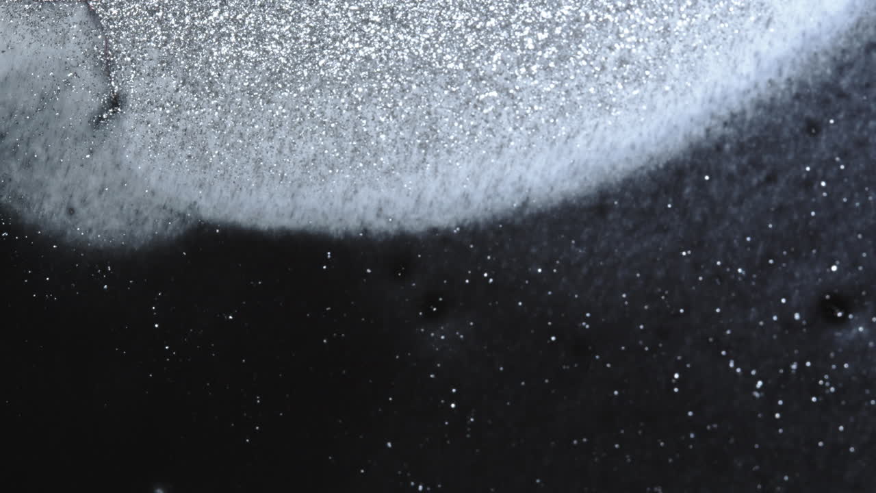 검은색에 반이는 은 입자의 신비한 클로즈업, 우주적인 분위기를 창조합니다.