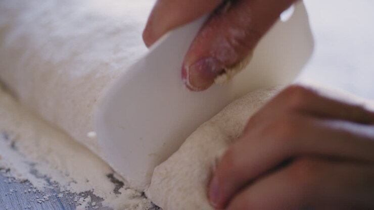 Close-up of male hands using dough scraper to cut through bread dough