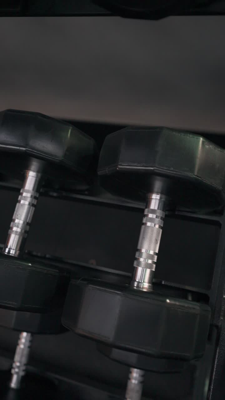 Athletic man in gym pick up and putting heavy dumbbells back onto storage rack - close- up shot