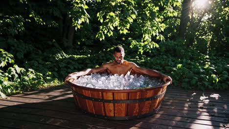 young athlete recovering in wooden tub, surrounded by lush greenery, experiencing cold therapy benefits amid serene natural setting during summer day