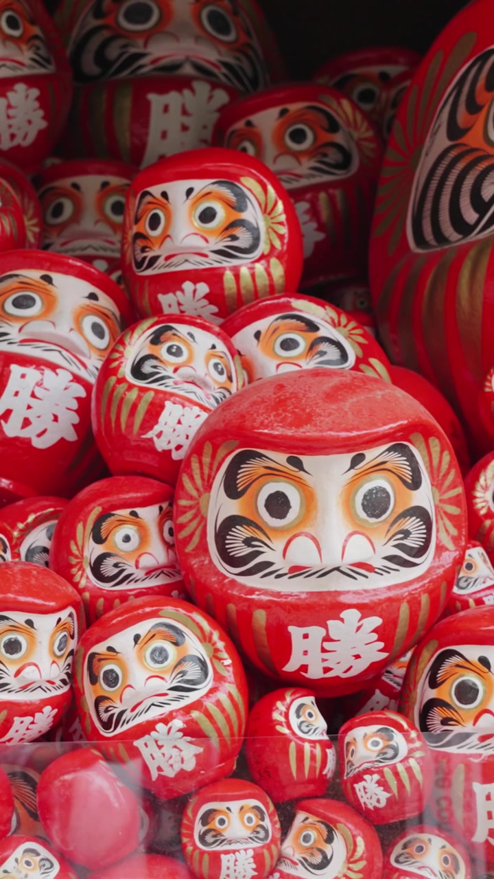 Primo piano verticale di centinaia di bambole Daruma rosse esposte al Tempio Katsuoji a Osaka, Giappone, che mostrano un simbolo tradizionale giapponese associato a buona fortuna, perseveranza, desideri e successo.