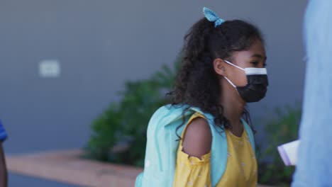 diverse male teacher measuring temperature of schoolchildren, all wearing face masks