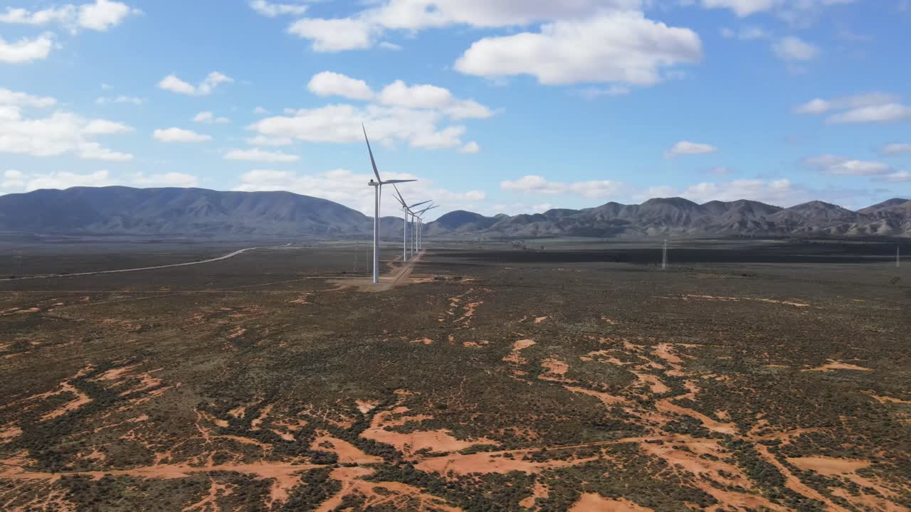 antena de drones moviéndose hacia un parque eólico de energía renovable en el desierto de australia con montañas en el fondo en un día de verano