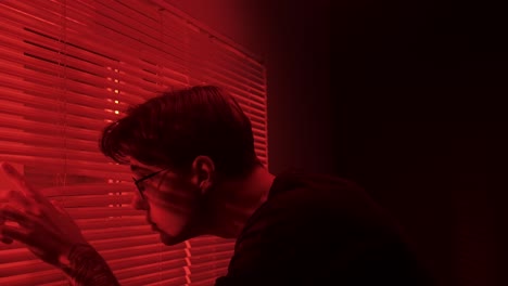 man looking through red lit blinds