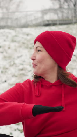 woman performs outdoor workout with hand up for balance turning left and right for coordination and strength on snowy ground wearing red hoodie and black gloves under foggy atmosphere