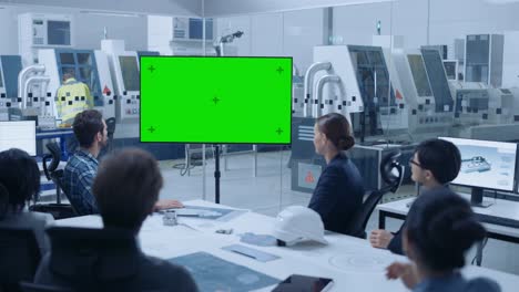 sala de oficinas de fábrica moderna: equipo diverso de ingenieros, gerentes e inversores sentados en la mesa de reuniones, saludan a la televisión interactiva que muestra pantalla verde videoconferencia de llamada