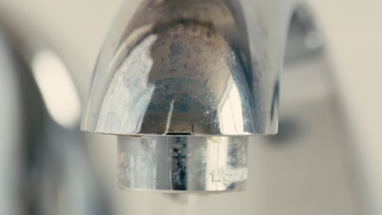 Primo piano di goccioline d'acqua che gocciolano lentamente da un rubinetto cromato del bagno durante il giorno