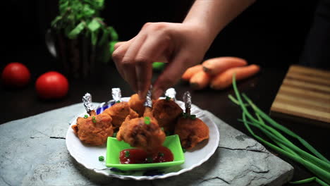 the chef dipping a piece of cooked chicken lollipop into tomato sauce and eating