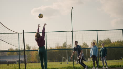 back view of lady playing volleyball with coach jumping and slamming ball across net, two amateurs watching in background, showcasing action, teamwork, and athleticism in volleyball practice