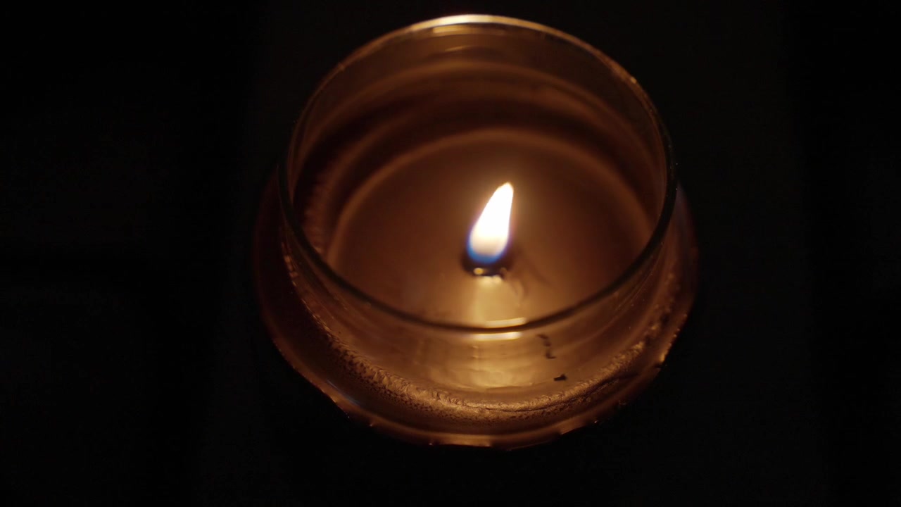 Una vela emite un brillo suave y cálido en un ambiente oscuro. La llama parpadeante crea una atmósfera relajante.