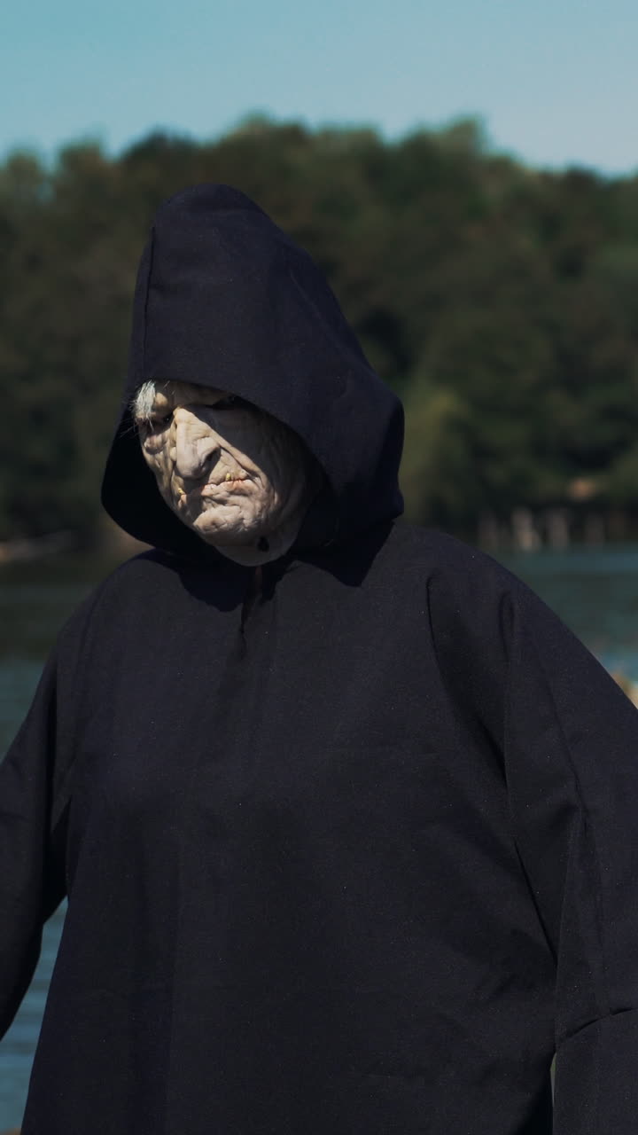 Eerie witch on river bank watches the camera. Halloween costume.. Vertical video
