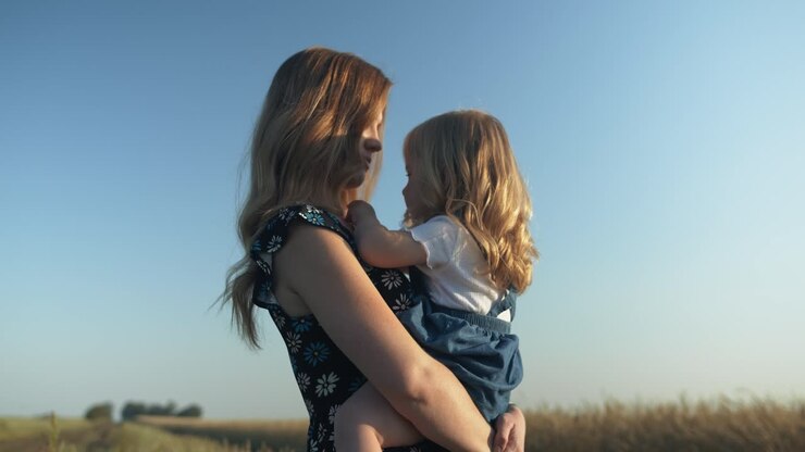 Happy mother holding and kissing her daughter together outside in summer having positive, loving family or mothers day moment in cinematic slow motion showing joys of motherhood