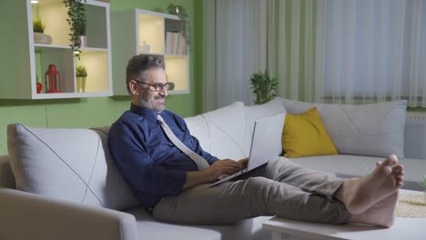 hombre usando una computadora portátil en el sofá relajándose en casa.