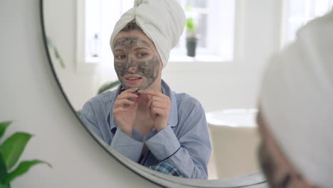 woman removes facial mask looking to the mirror