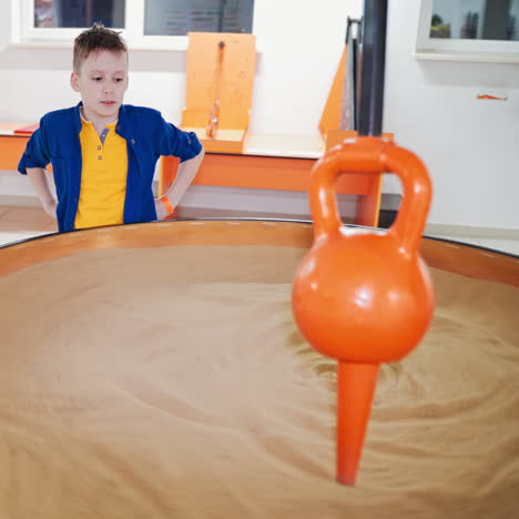 boy visiting a science museum for children. he plays with a sand pendulum