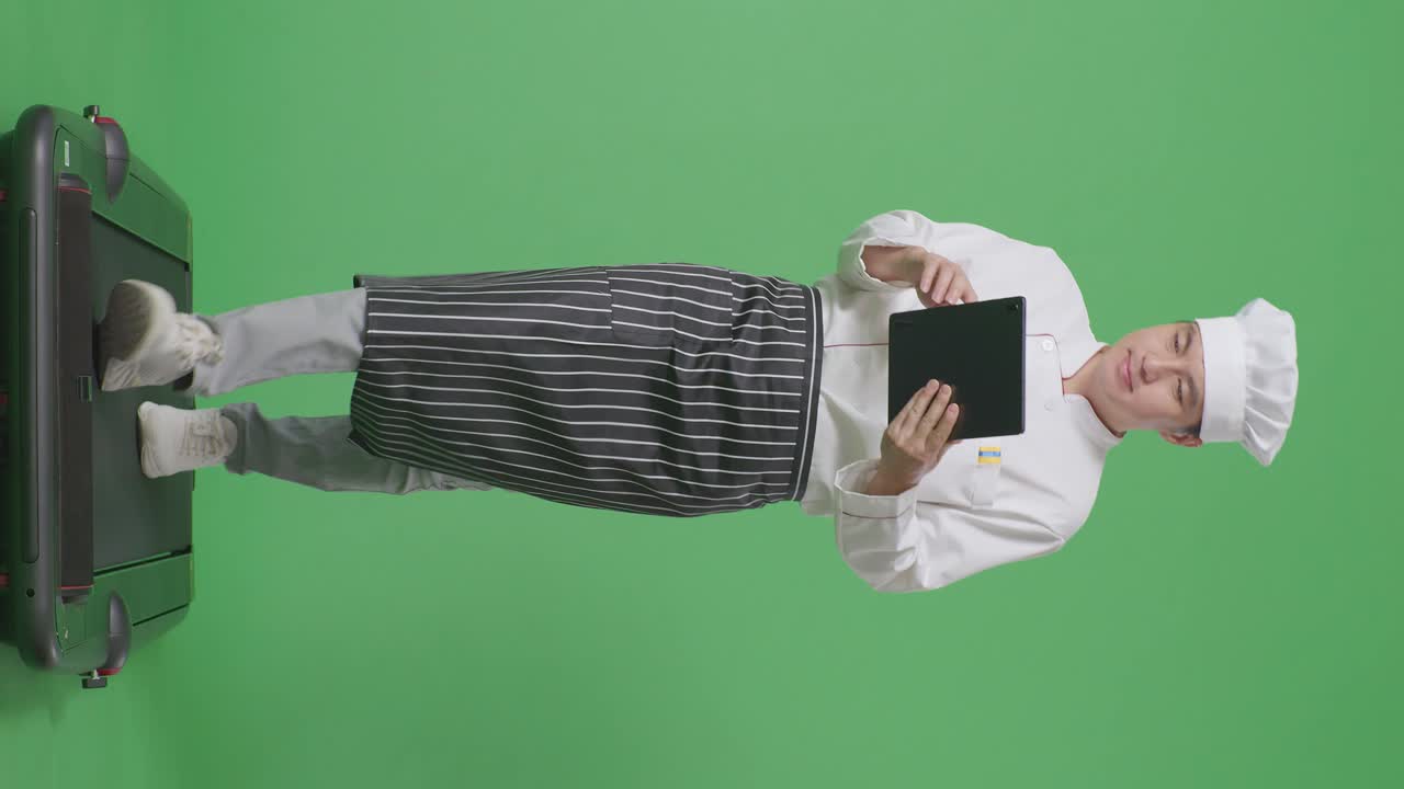 Chef uomo asiatico a figura intera che usa un tablet mentre cammina sul tapis roulant nello studio con sfondo verde.