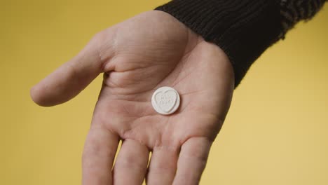 Close-Up-Of-Hand-Holding-Heart-Candy-With-All-Yours-Message-On-Yellow-Background