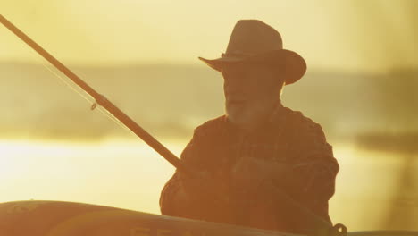 close-up view of a senior caucasian man floating with oars in a boat in the dawn in the middle of the lake