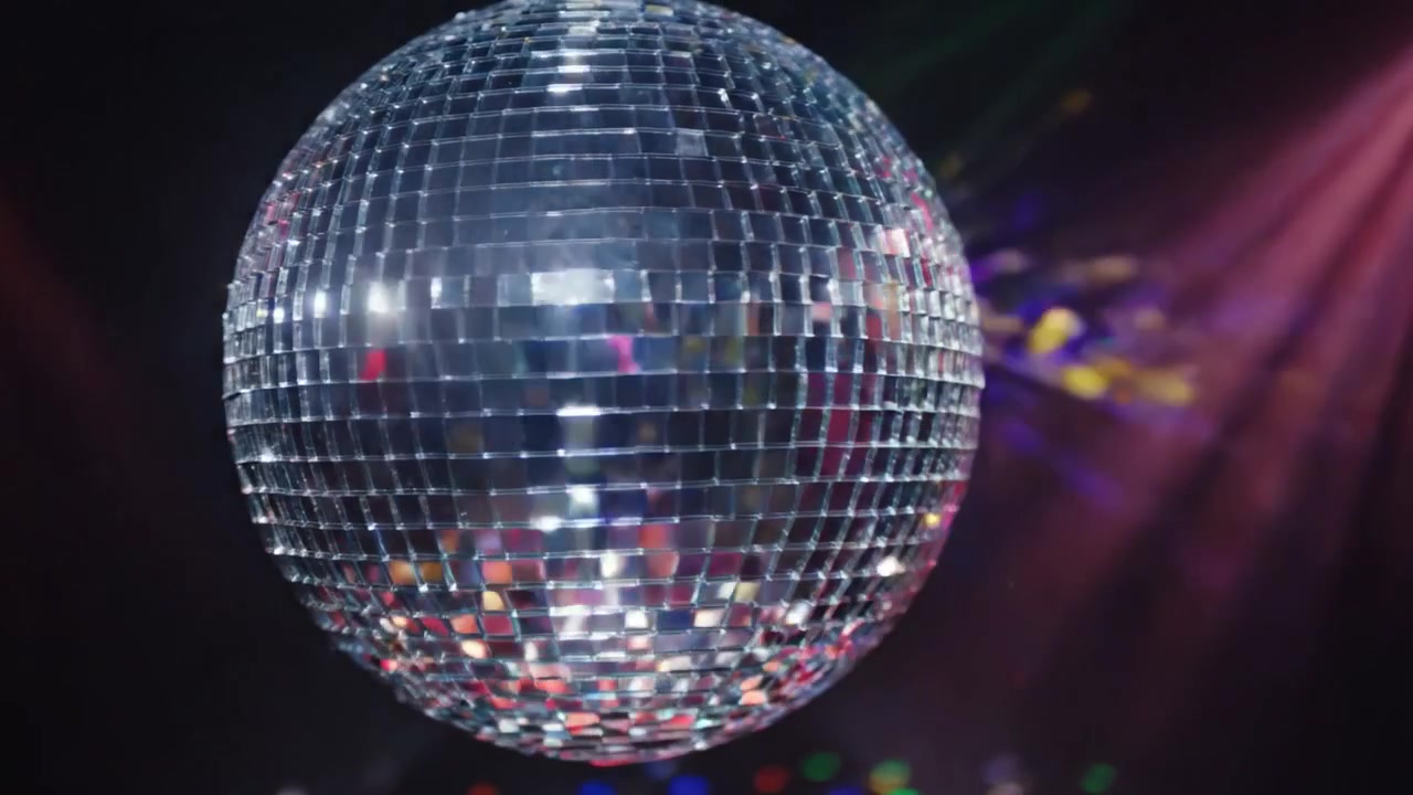 En fængslende scene med en glitrende diskokugle, der drejer let under farverige scenelys, hvilket skaber blændende refleksioner på dansegulvet for en levende atmosfære