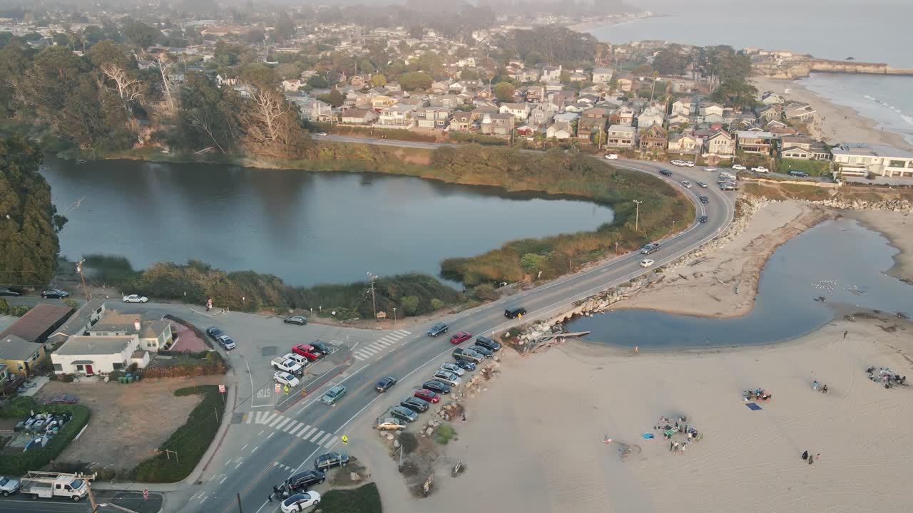 A slow-motion drone shot strafing a road near a peaceful, beachside Santa Cruz California community with expensive residential houses and short term rentals next to the small craft harbor at sunset