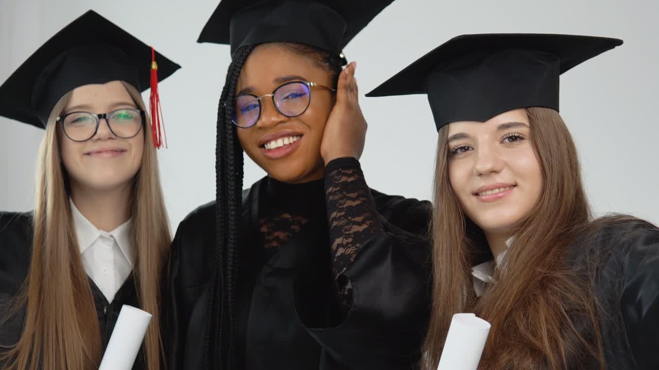 tres jóvenes graduadas felices de diferentes nacionalidades están juntas uno al lado del otro con diplomas en las manos. vista de cerca sobre fondo blanco