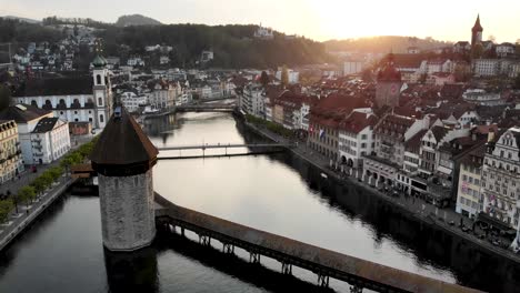 Vista-Aérea-De-Lucerna,-Suiza-Mientras-Se-Mueve-Desde-El-Puente-Kappelbrücke-Hacia-La-Puesta-De-Sol-Detrás-Del-Histórico-Altstadt