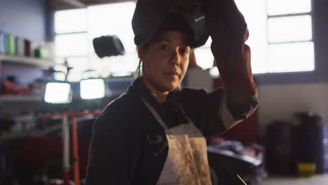 Portrait-of-female-mechanic-removing-welding-helmet-at-a-car-service-station