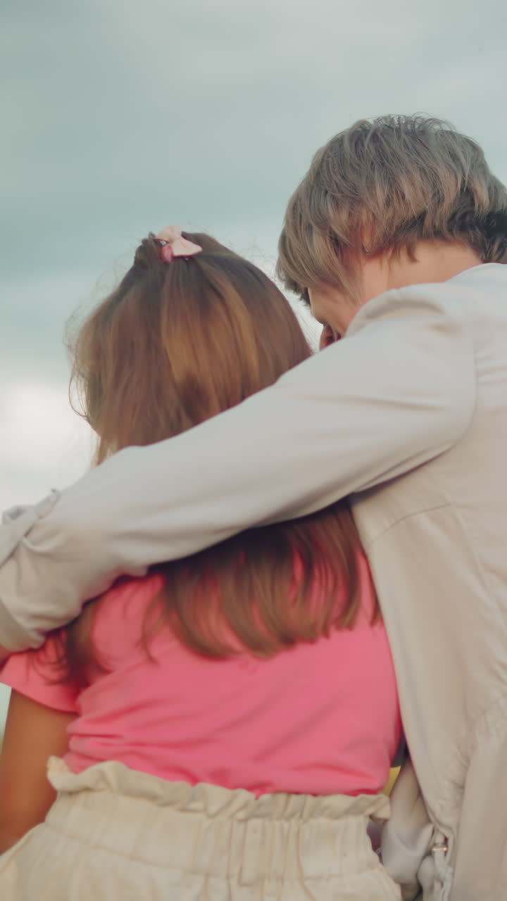 vista trasera de una mujer abrazando a una niña en una bala de heno, ambos absortos en una novela, bajo un cielo nublado, que representa un momento sereno y de unión en un campo abierto