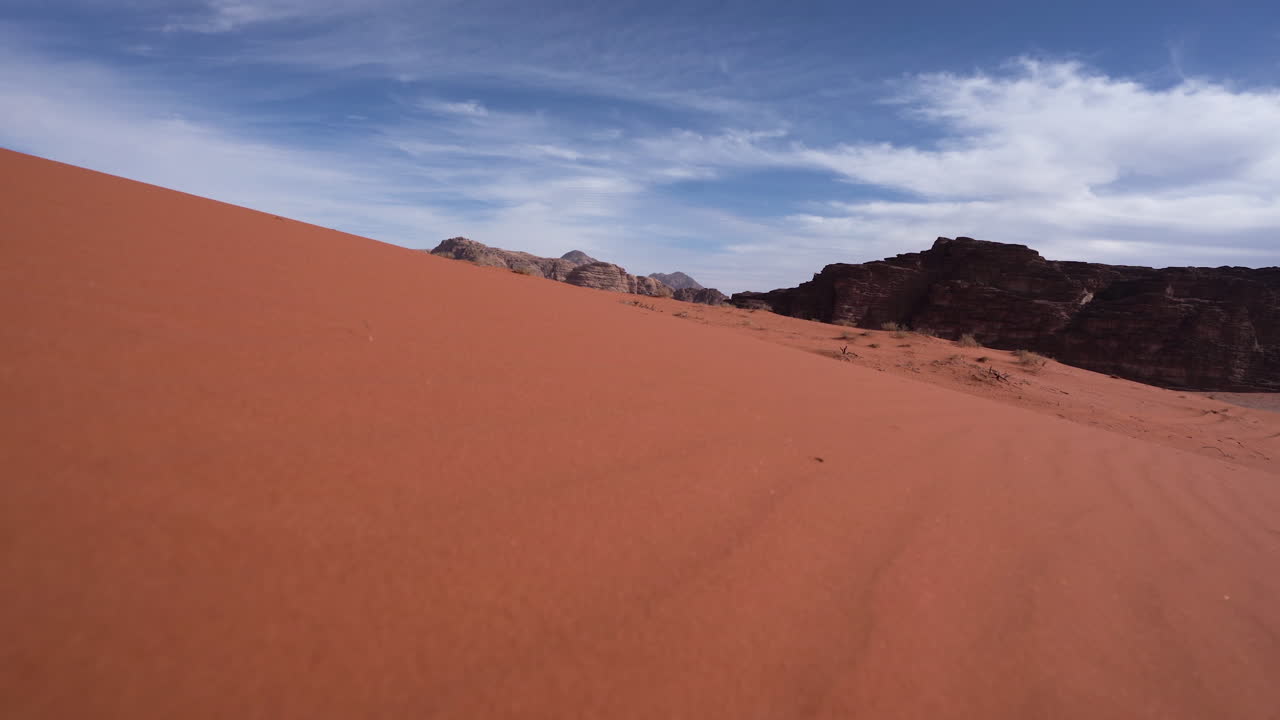 배경에 산과 모래 풀이 보이는 모래 언덕에서 내리막 길을 걷다