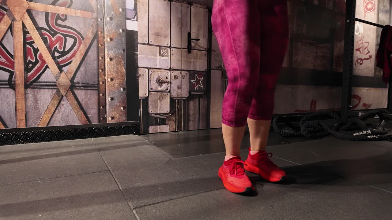 Close up, low angle view of a fit woman's feet in red sneakers skipping with a jump rope. Cardio workout and fitness training in a modern gym