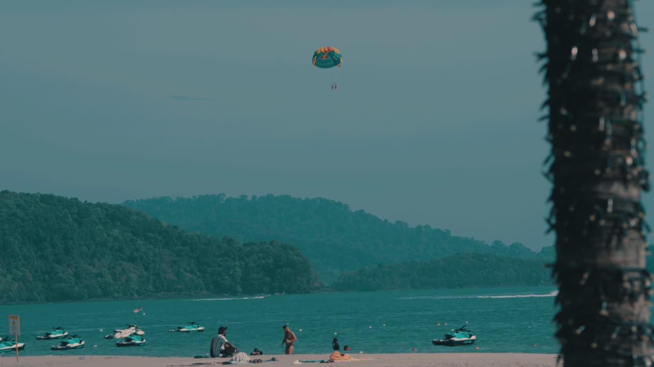 Parasailing over a beach with boats and hills in Langkawi, Malaysia, tropical adventure