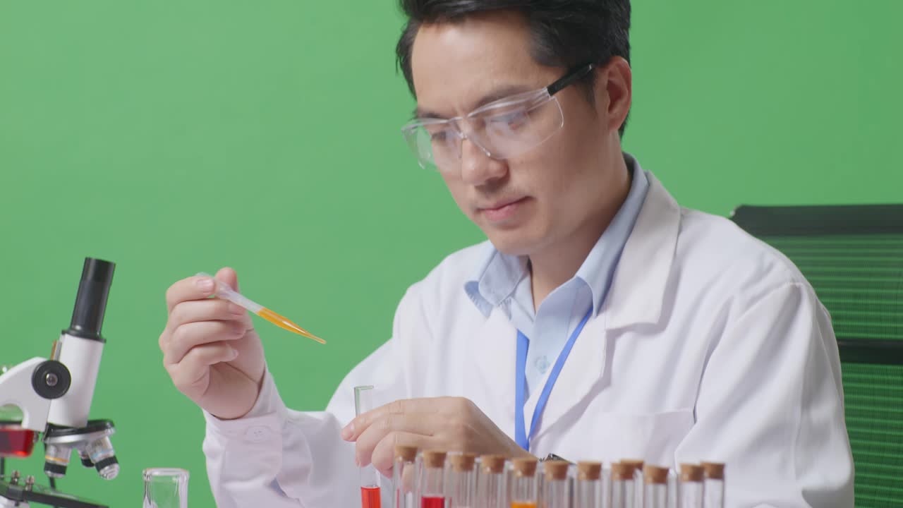 Close Up Of Side View Of Asian Man Scientist Sitting And Making Experiment With Test Tube On The Table With Microscope In The Green Screen Background Laboratory