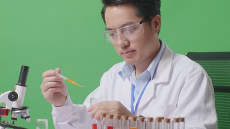 close up of side view of asian man scientist sitting and making experiment with test tube on the table with microscope in the green screen background laboratory